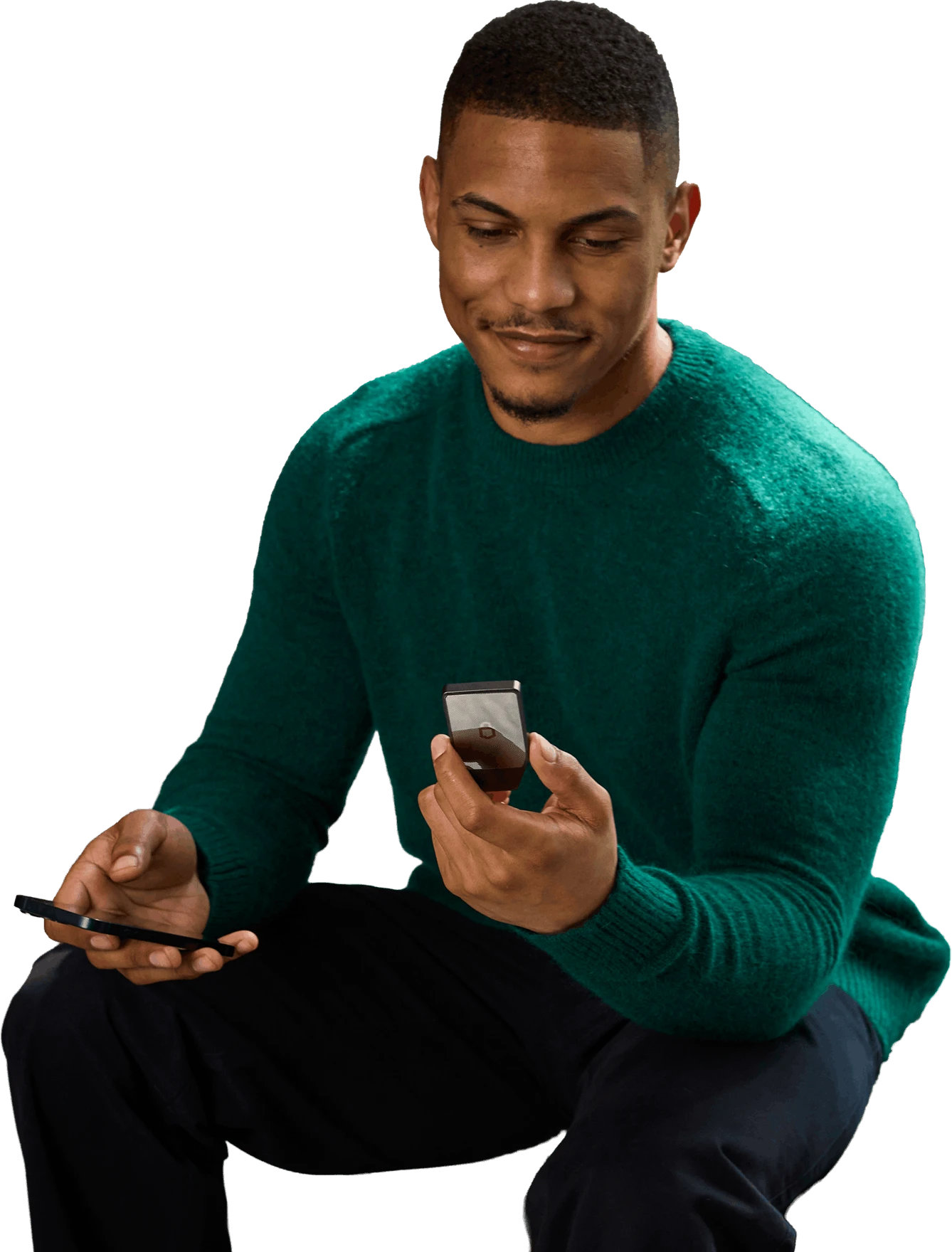 Man in a green sweater sitting and smiling while holding a Trezor Safe 7 hardware wallet and a smartphone.